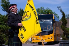 Man dressed in a kilt holding a yellow flag infront of Gordon Highlander coach